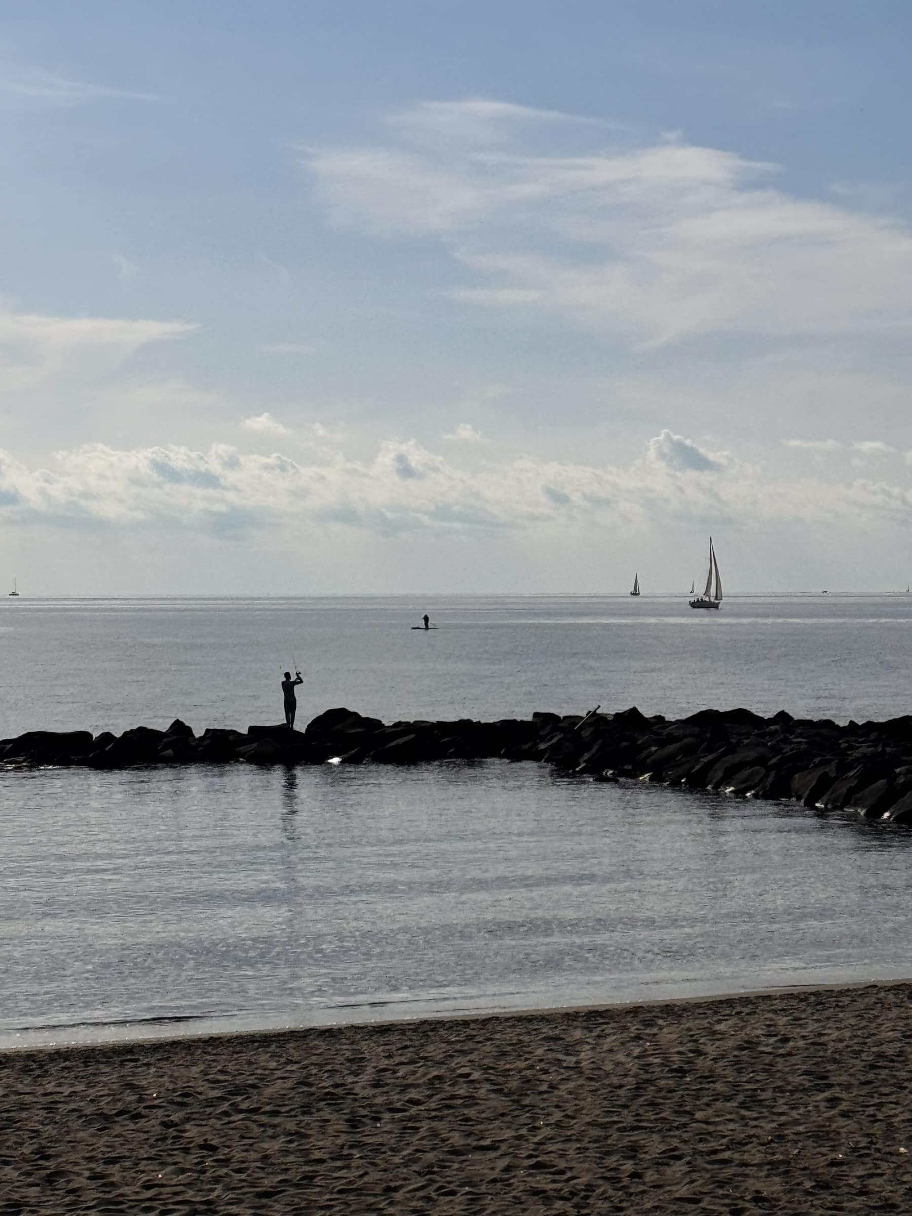 Spiaggia di Ostia con un pescatore e una vela in lontananza